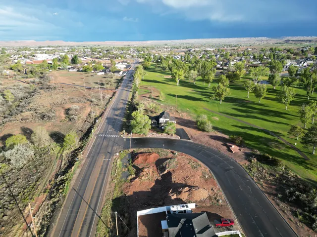 Aerial perspective showcasing a residential area with a prominent paved road, landscaped green space with mature trees, and a distant mountain range looking SOUTH EAST