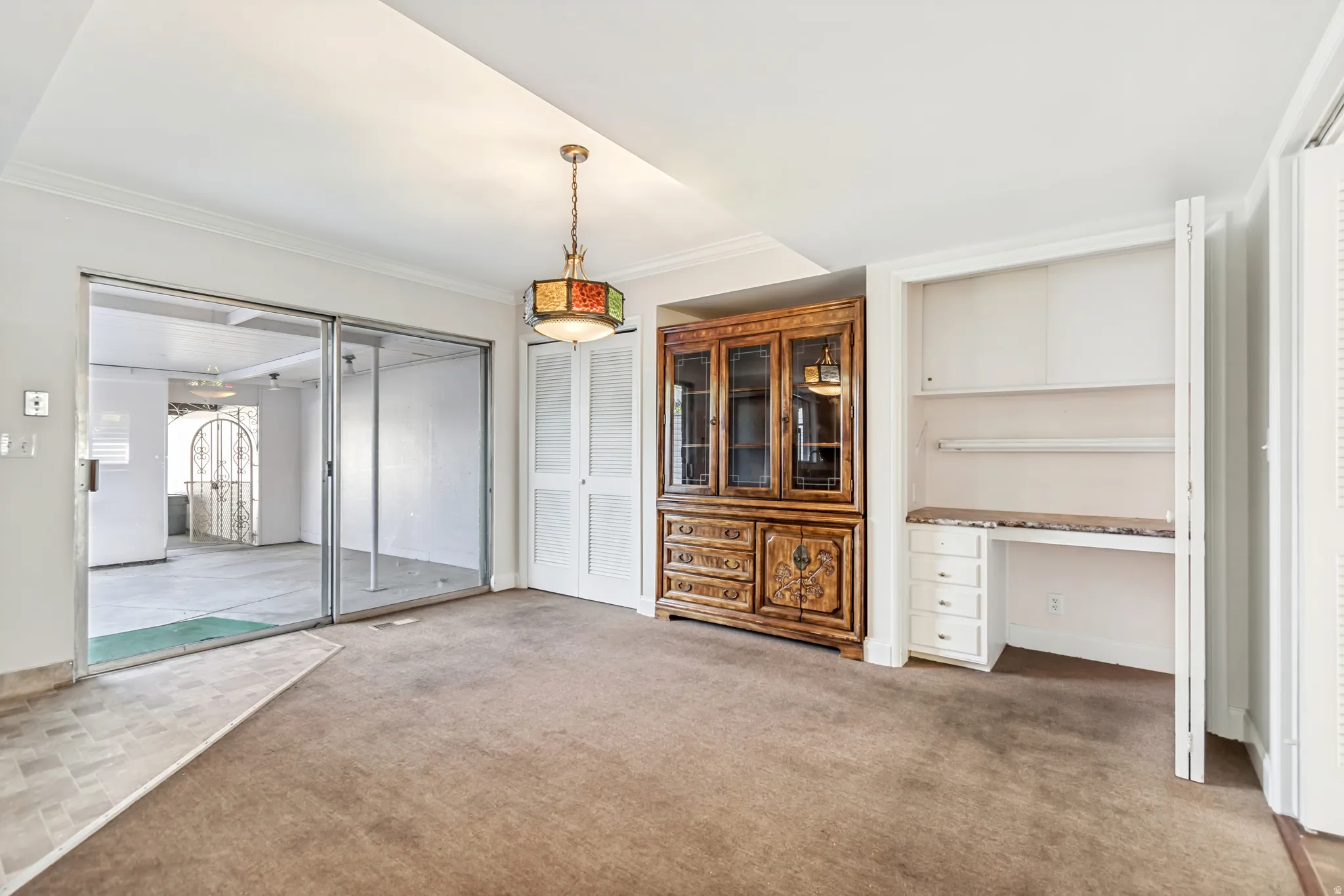 Carpeted interior space featuring a built-in desk with shelving, an ornamental stained-glass style ceiling fixture, and bi-fold closet doors