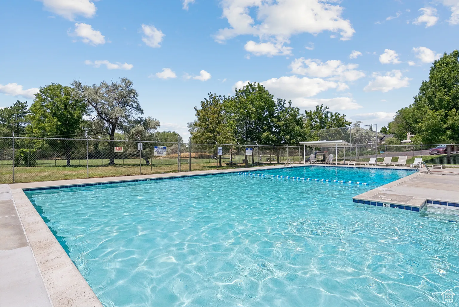 Outdoor swimming pool featuring a perimeter fence, concrete deck, and shade structure