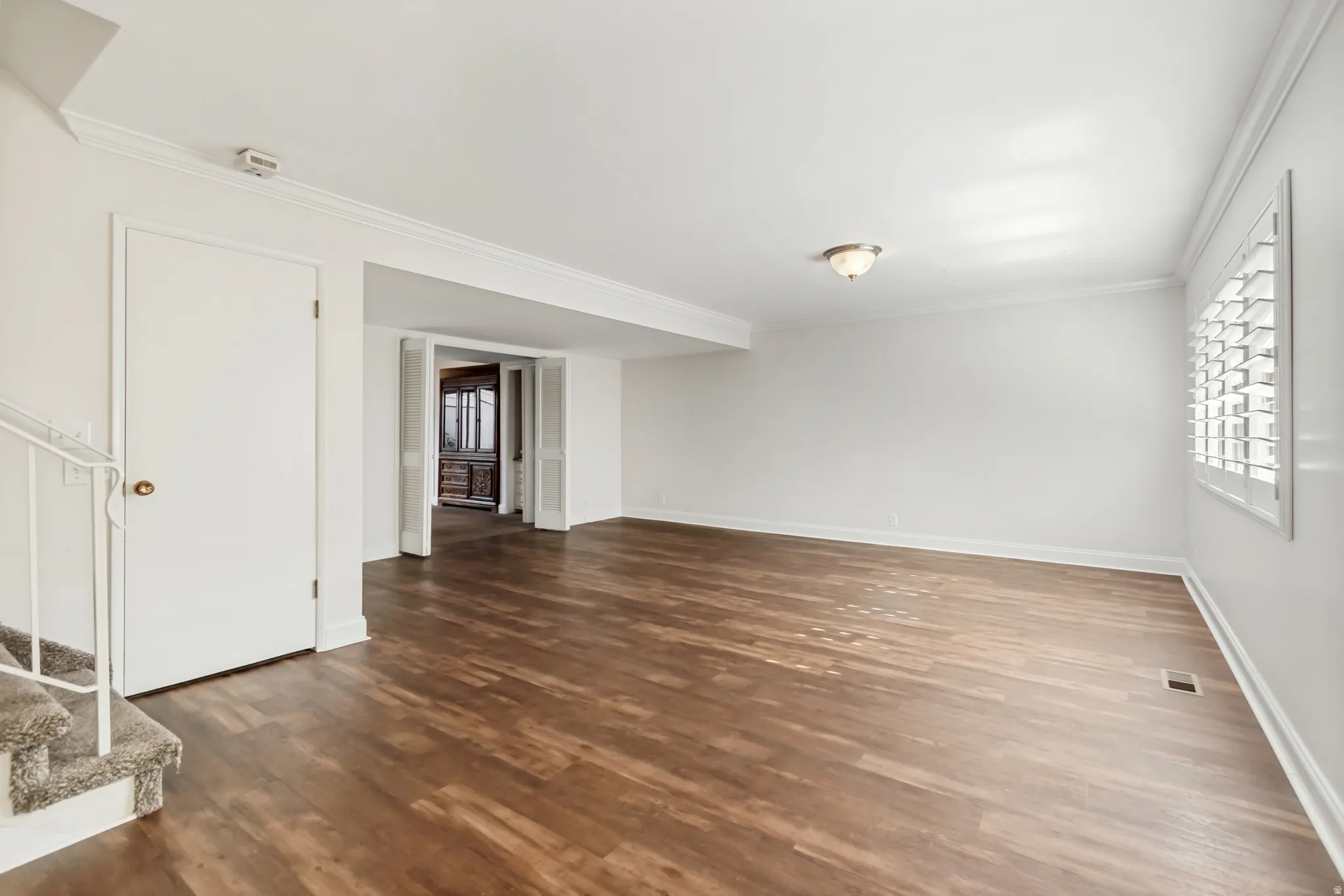Spacious room featuring wood-finish flooring, white walls, and crown molding