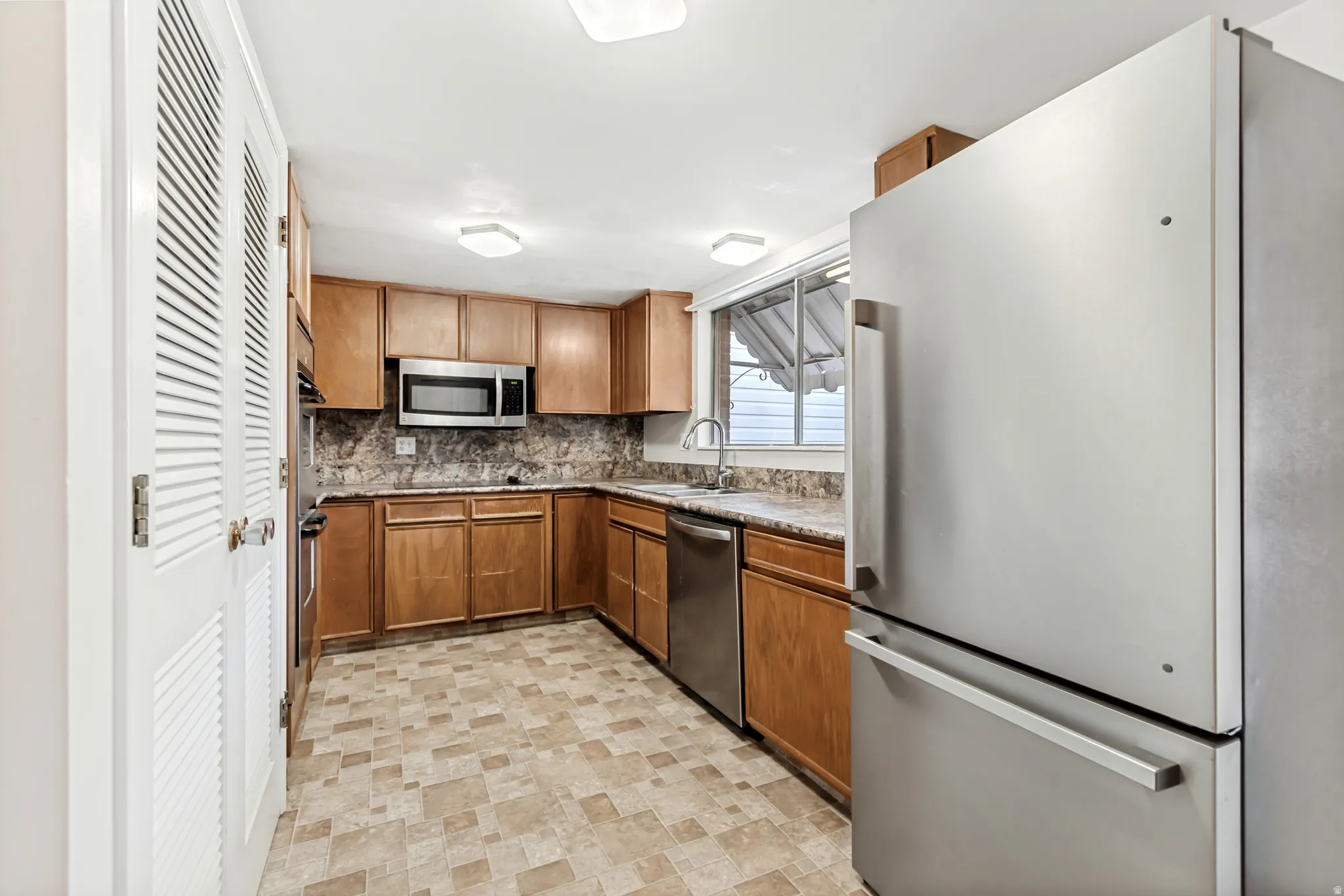 Kitchen featuring wood cabinetry, stainless steel appliances, patterned flooring, and a window above the sink