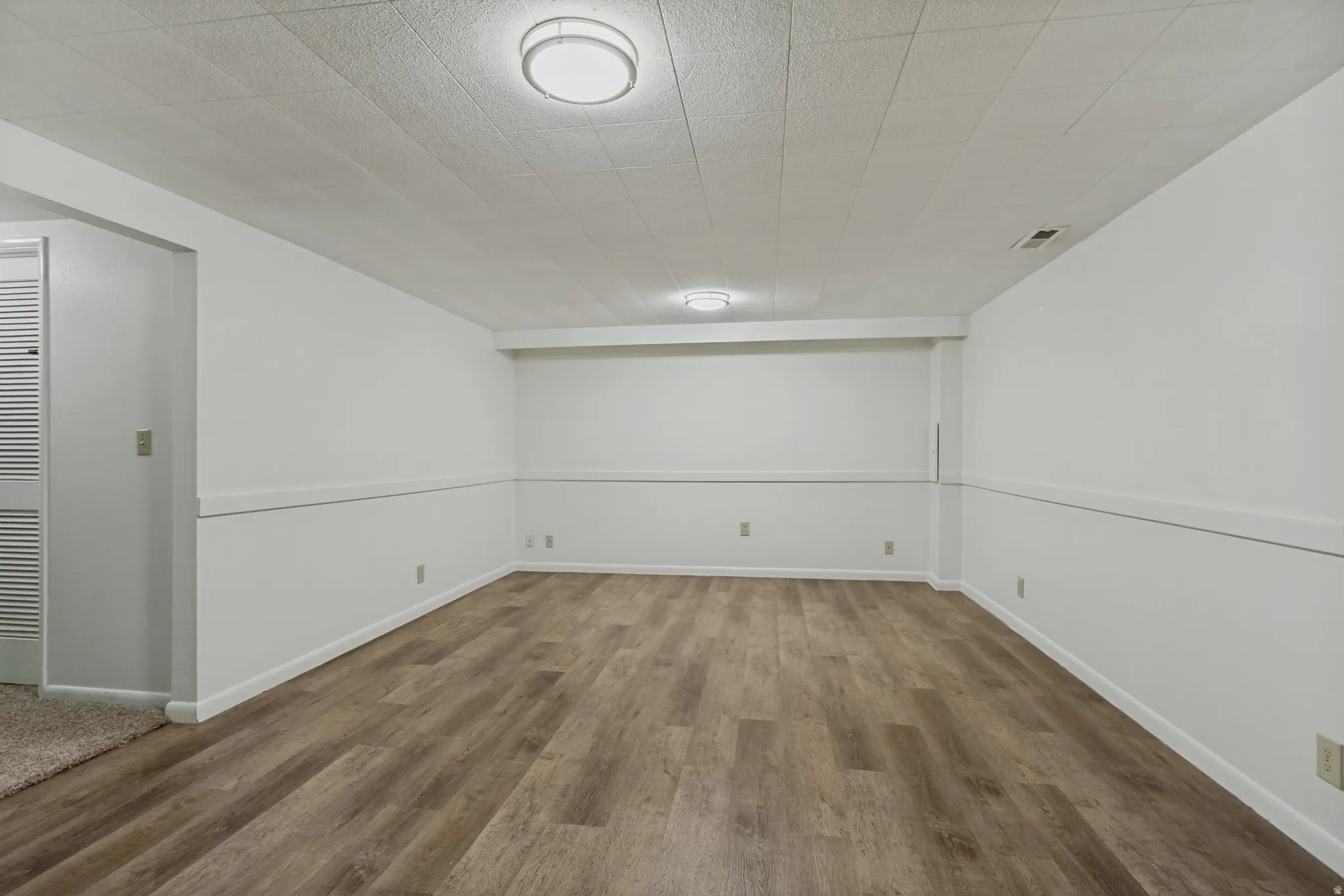 Spacious room featuring wood-finish flooring, white walls, and recessed lighting