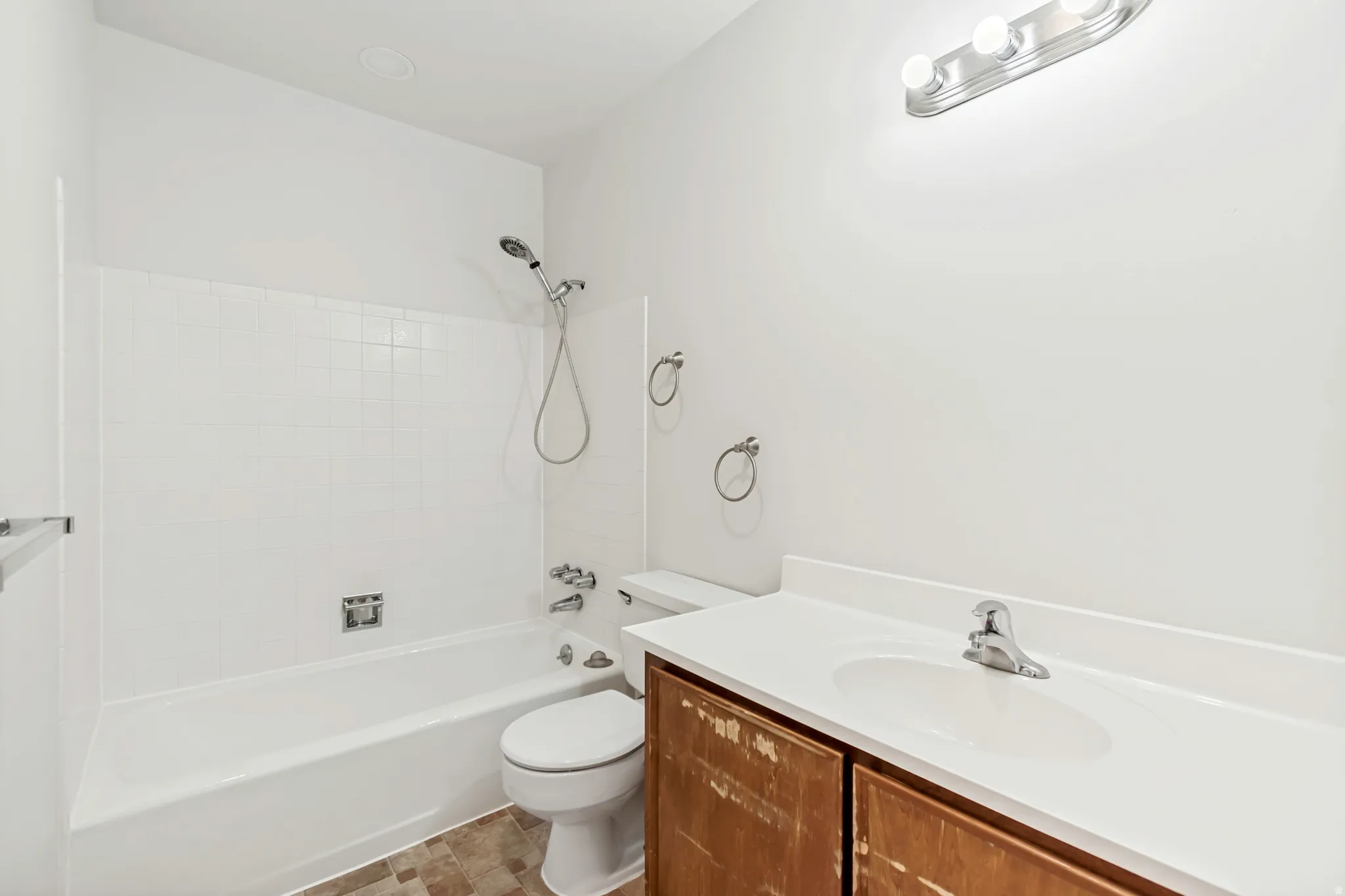 Full bathroom featuring a white tub with shower head, white tiled surround, and a white toilet