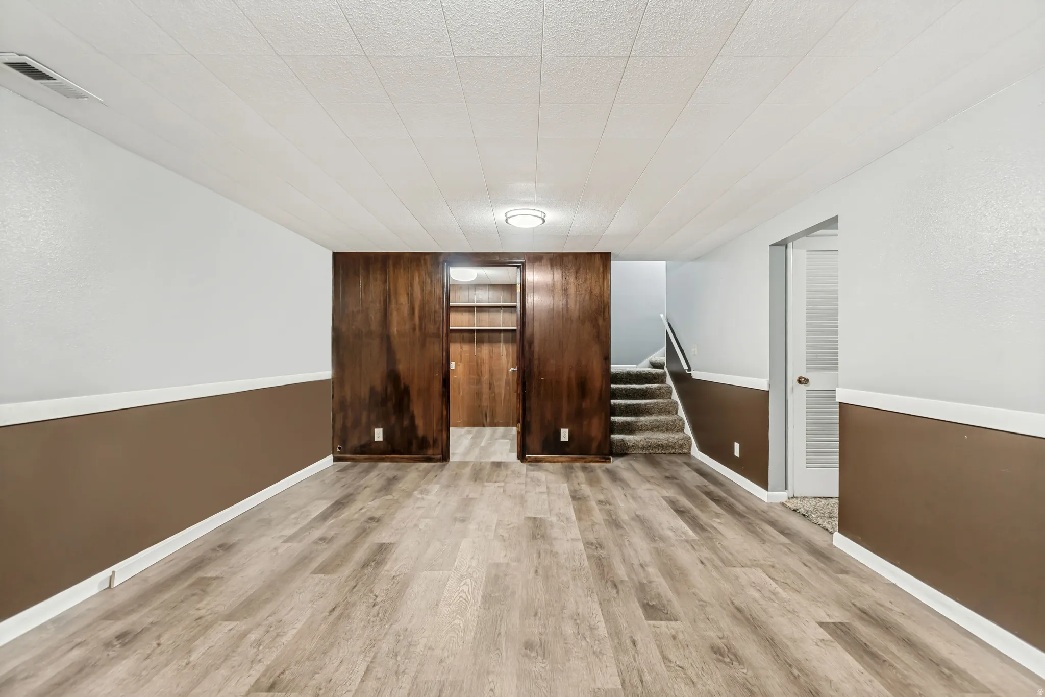 Spacious room featuring wood-finish flooring, two-tone wall paint, a drop ceiling, and recessed lighting