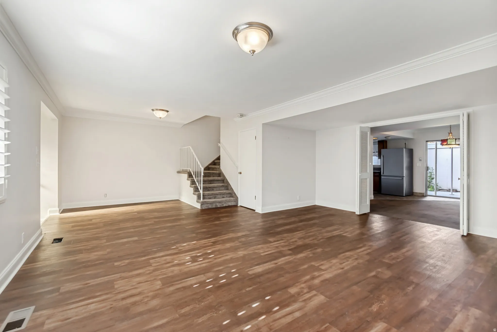 Spacious room featuring wood-finish flooring, white walls, and crown molding