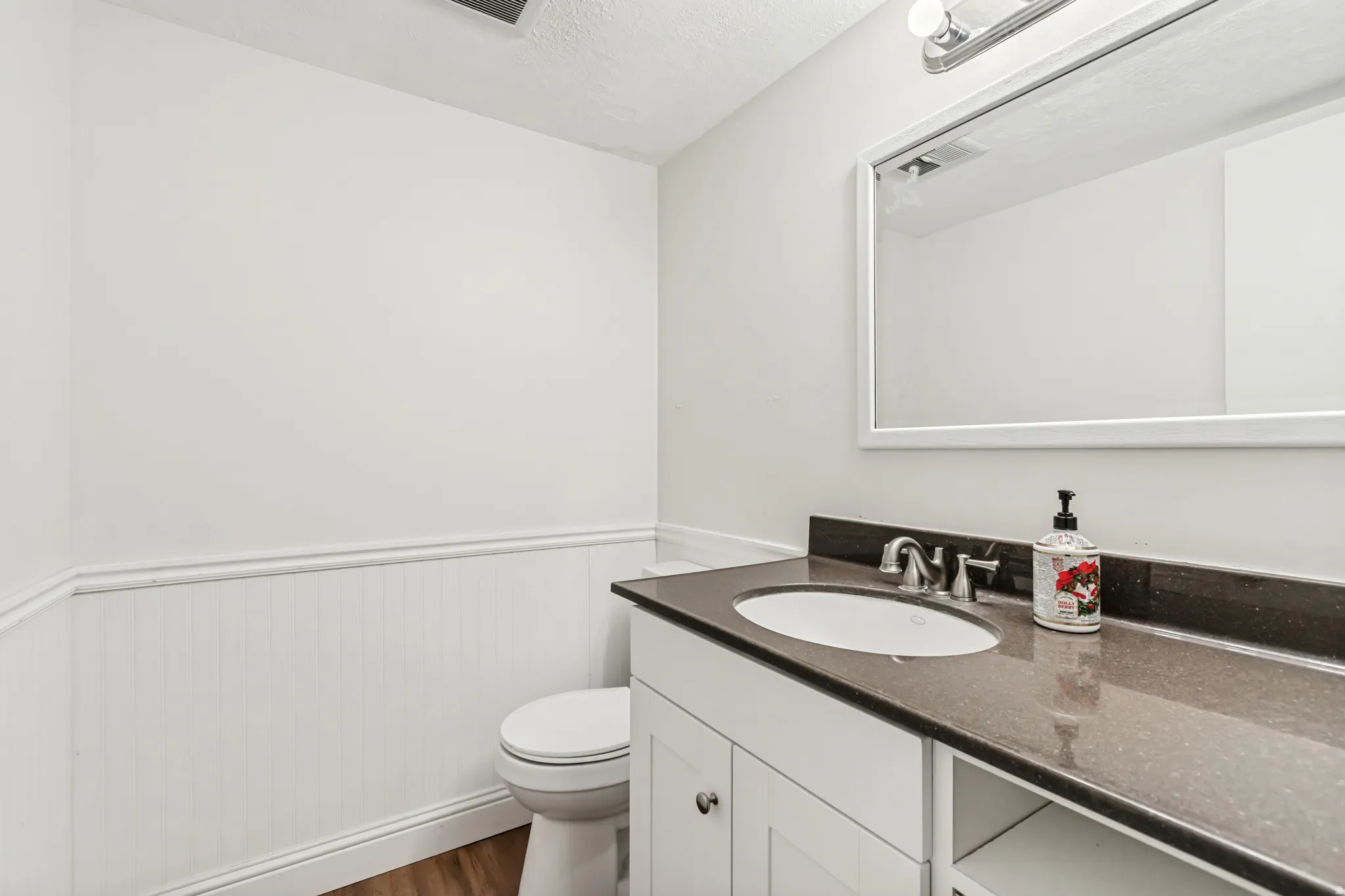 Powder room featuring a white vanity with a dark countertop, an undermount sink, and a framed mirror with overhead lighting