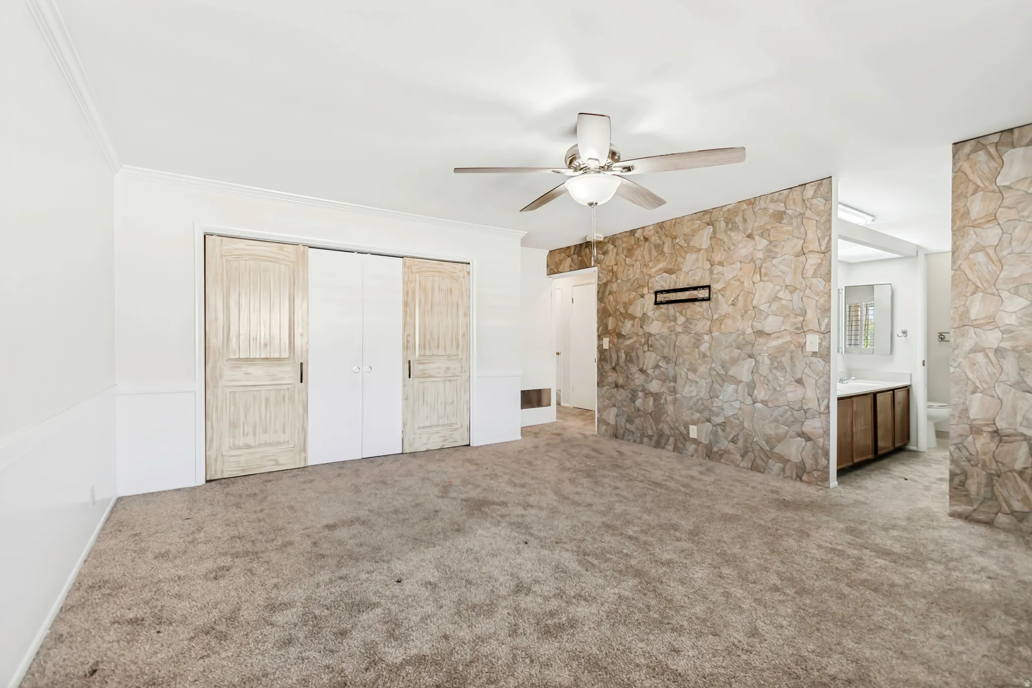 Spacious room featuring neutral carpet flooring, a ceiling fan with light fixture, and crown molding