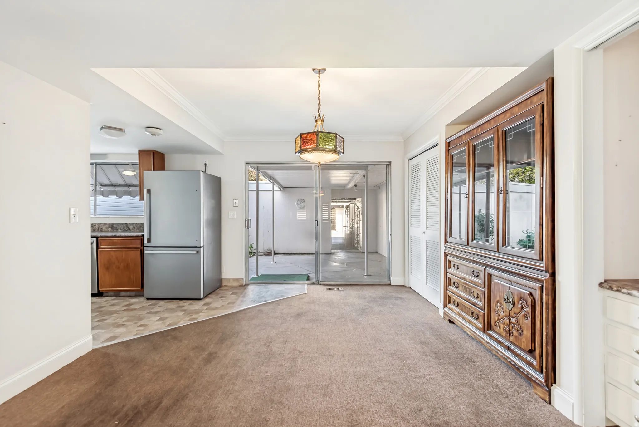 Carpeted common area featuring a kitchen alcove with tile flooring, a stainless steel refrigerator, and wood-finish cabinetry