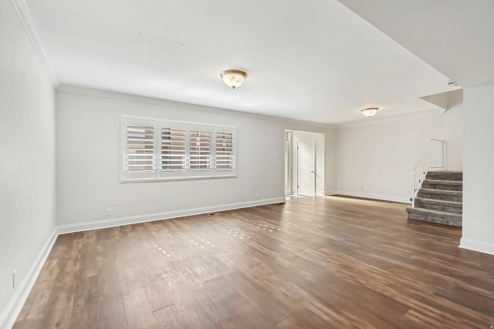 Spacious room featuring wood-finish flooring, white walls, and crown molding