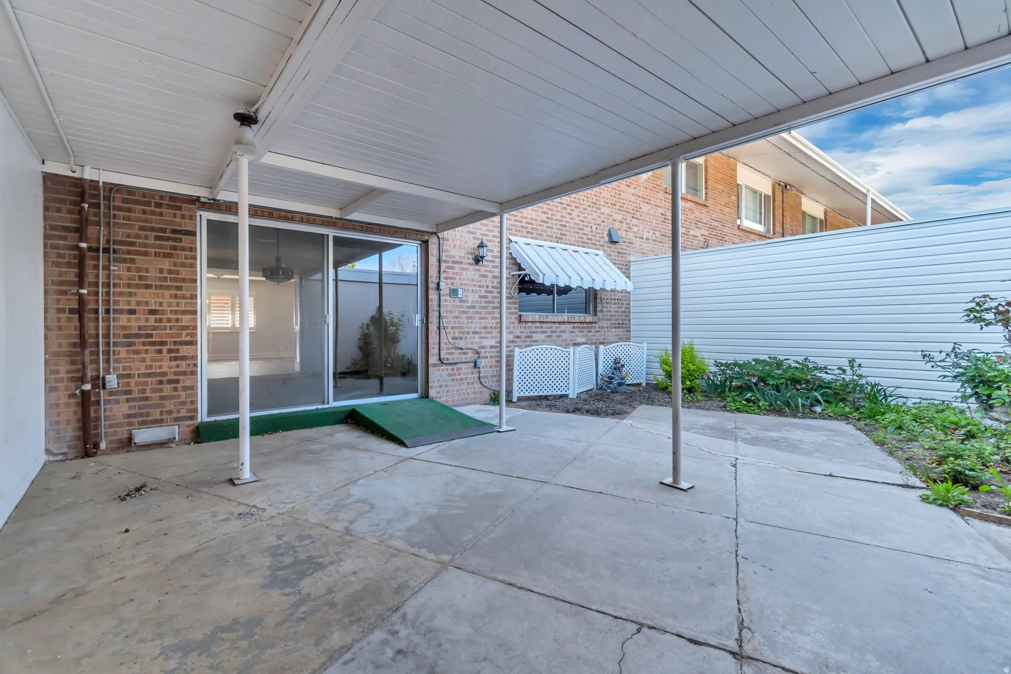 Covered concrete patio with a brick exterior, sliding glass door entry, and a window with an awning