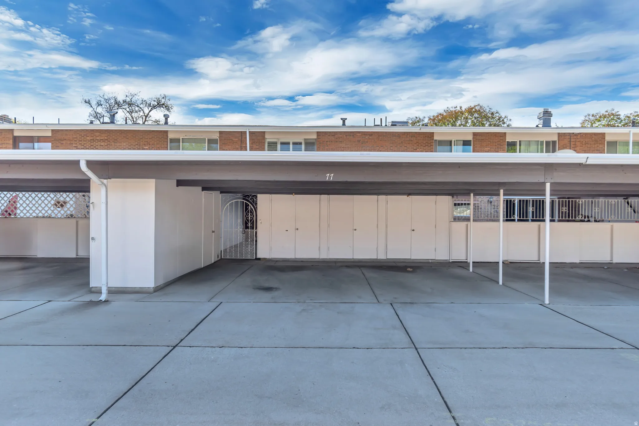 Covered parking structure with concrete ground, featuring multiple parking spaces and integrated storage closets