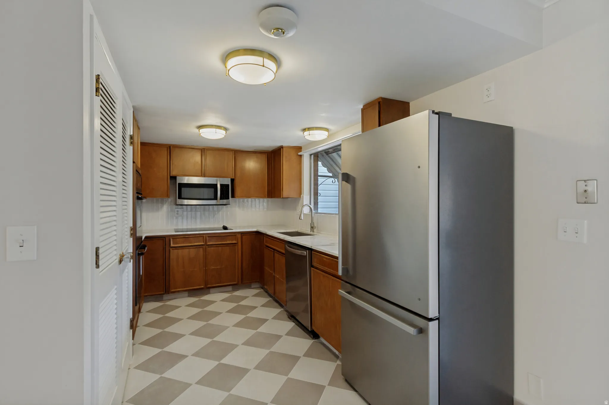 Kitchen featuring L-shaped wood cabinetry, stainless steel appliances, checkered tile flooring, and white countertops with a tile backsplash