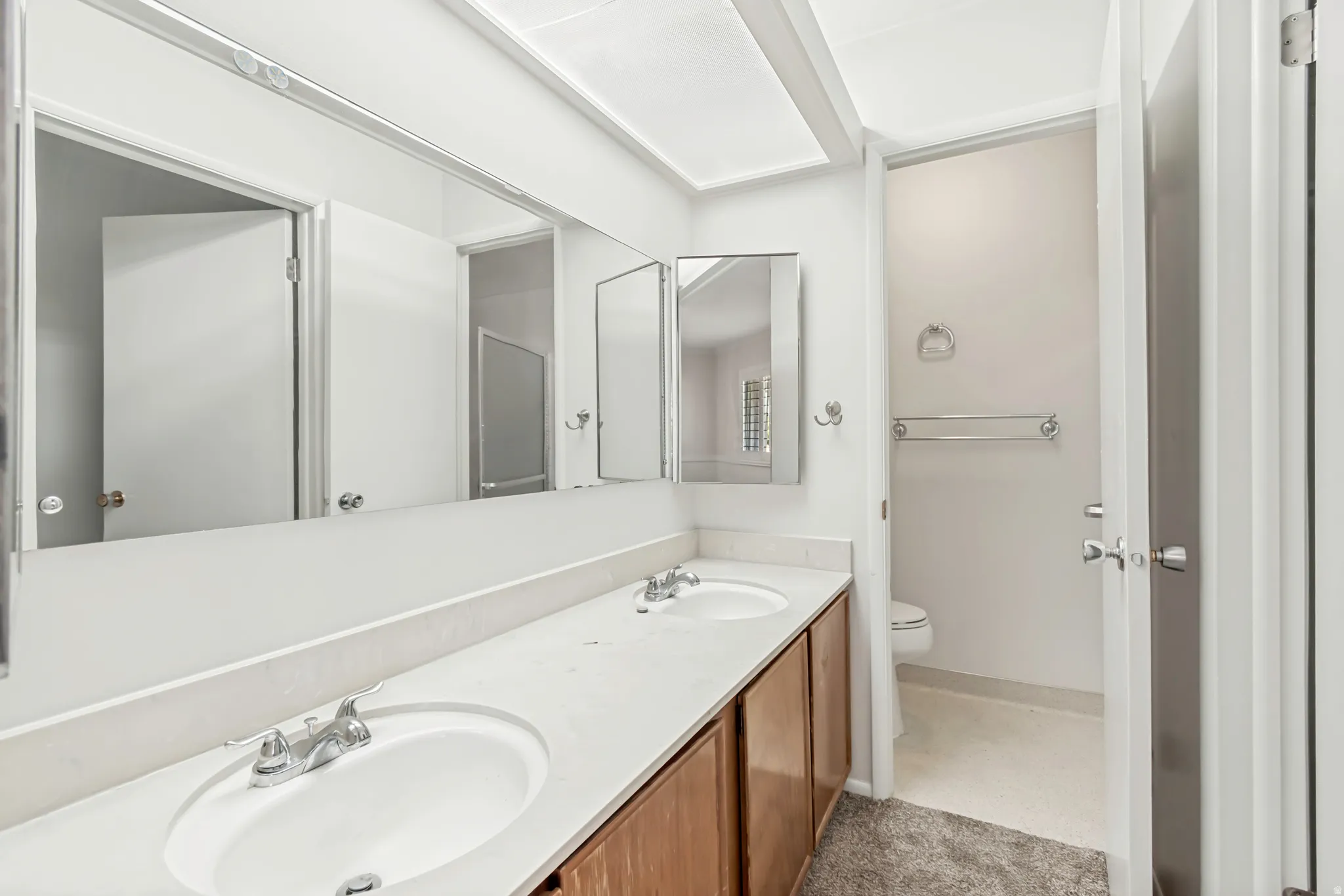 Dual vanity with integrated sinks, chrome faucets, wood-finish cabinetry, and a full-width wall mirror