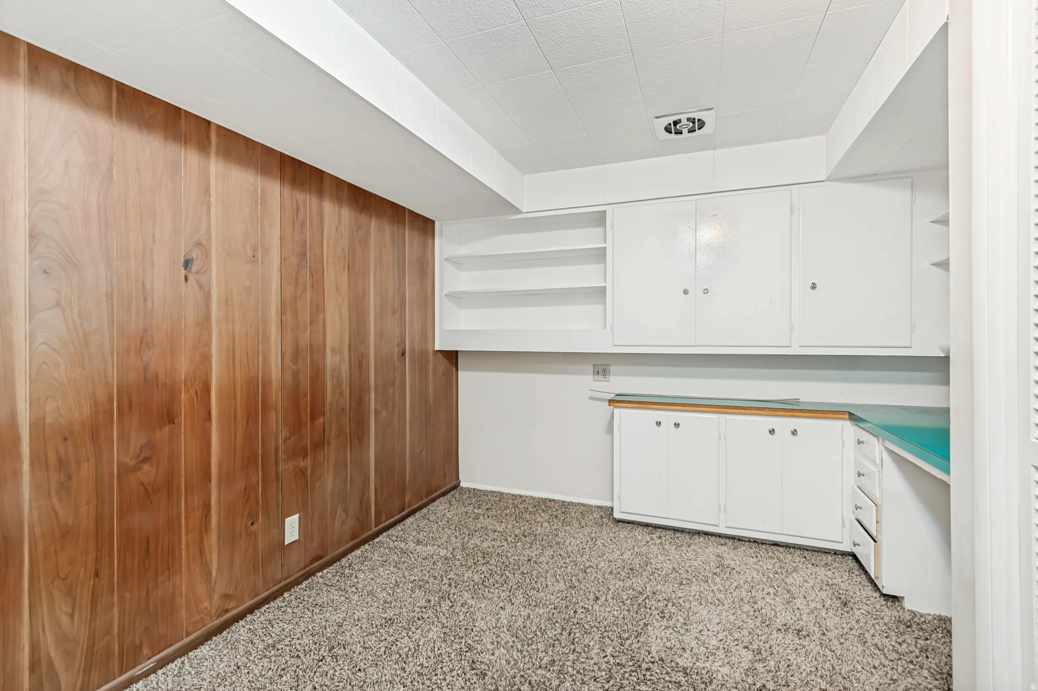 Room featuring wood paneling, built-in white cabinetry, open shelving, and a counter space with a teal surface