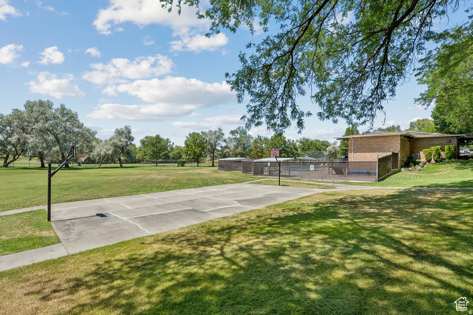 Concrete basketball court with dual hoops, surrounded by expansive green space and mature trees