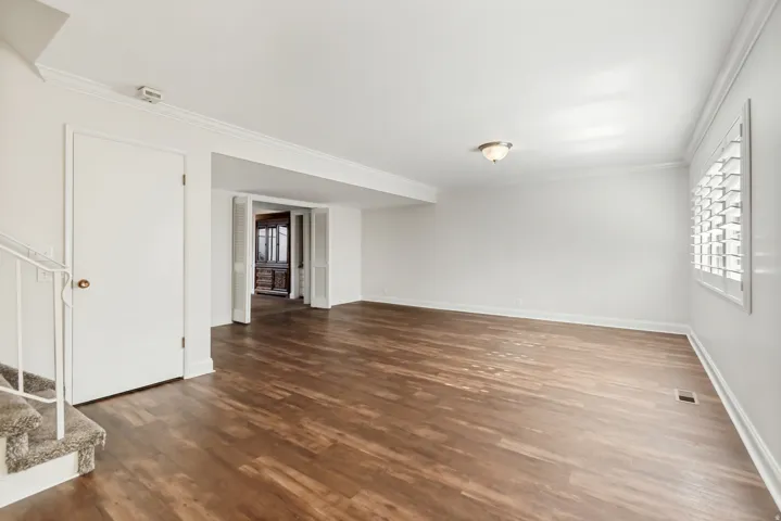 Spacious room featuring wood-finish flooring, white walls, and crown molding