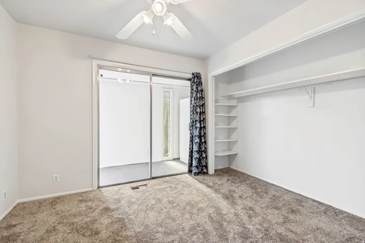 Carpeted interior space featuring a ceiling fan, sliding glass doors with an adjacent patterned curtain, and extensive built-in shelving