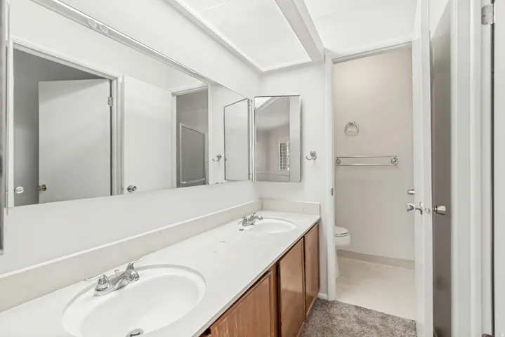 Dual vanity with integrated sinks, chrome faucets, wood-finish cabinetry, and a full-width wall mirror