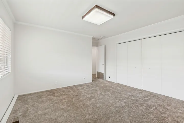 Spacious room featuring plush carpeting, white walls, and a large window with blinds