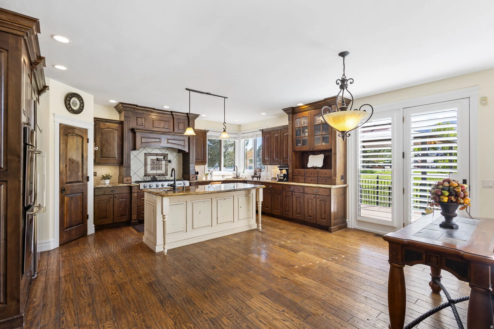 Kitchen featuring two tone color scheme, dark wood-style floors, an island with sink, hanging light fixtures, and light stone counters