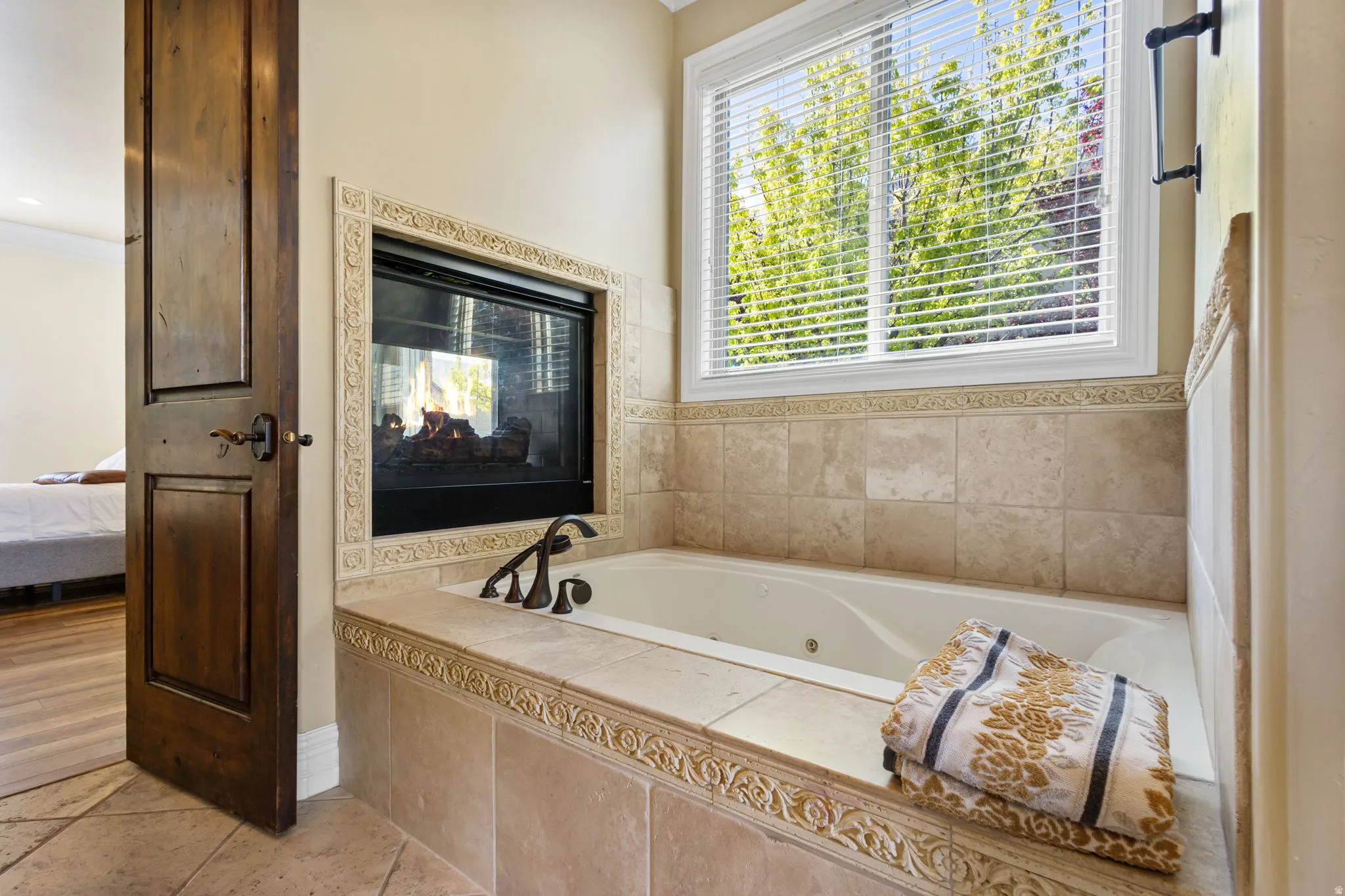 Full bathroom featuring a tub with jets, connected bathroom, a multi sided fireplace, ornamental molding, and light tile patterned floors