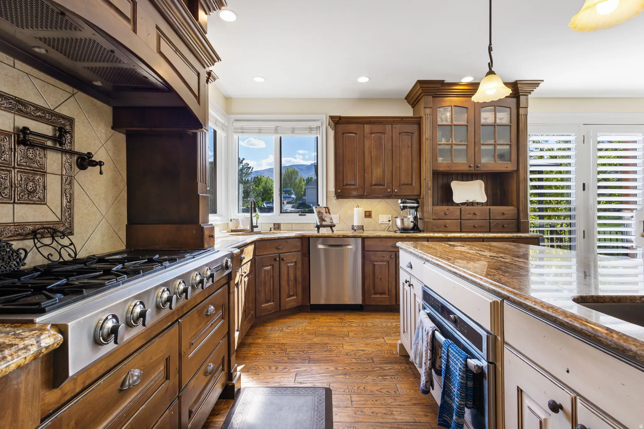 Kitchen featuring two tone cabinetry, dark stone counters, stainless steel appliances, dark wood-style floors, and glass fronted cabinets