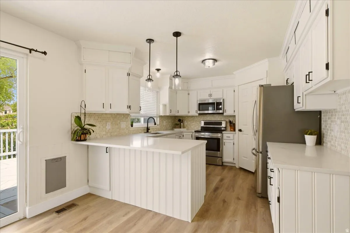 Kitchen featuring white cabinetry, stainless steel appliances, light countertops, and wood-finish flooring
