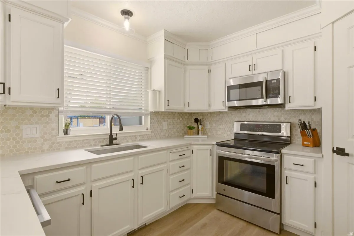 Modern kitchen featuring white cabinetry, quartz countertops, a honeycomb tile backsplash, stainless steel appliances, and wood-finish flooring