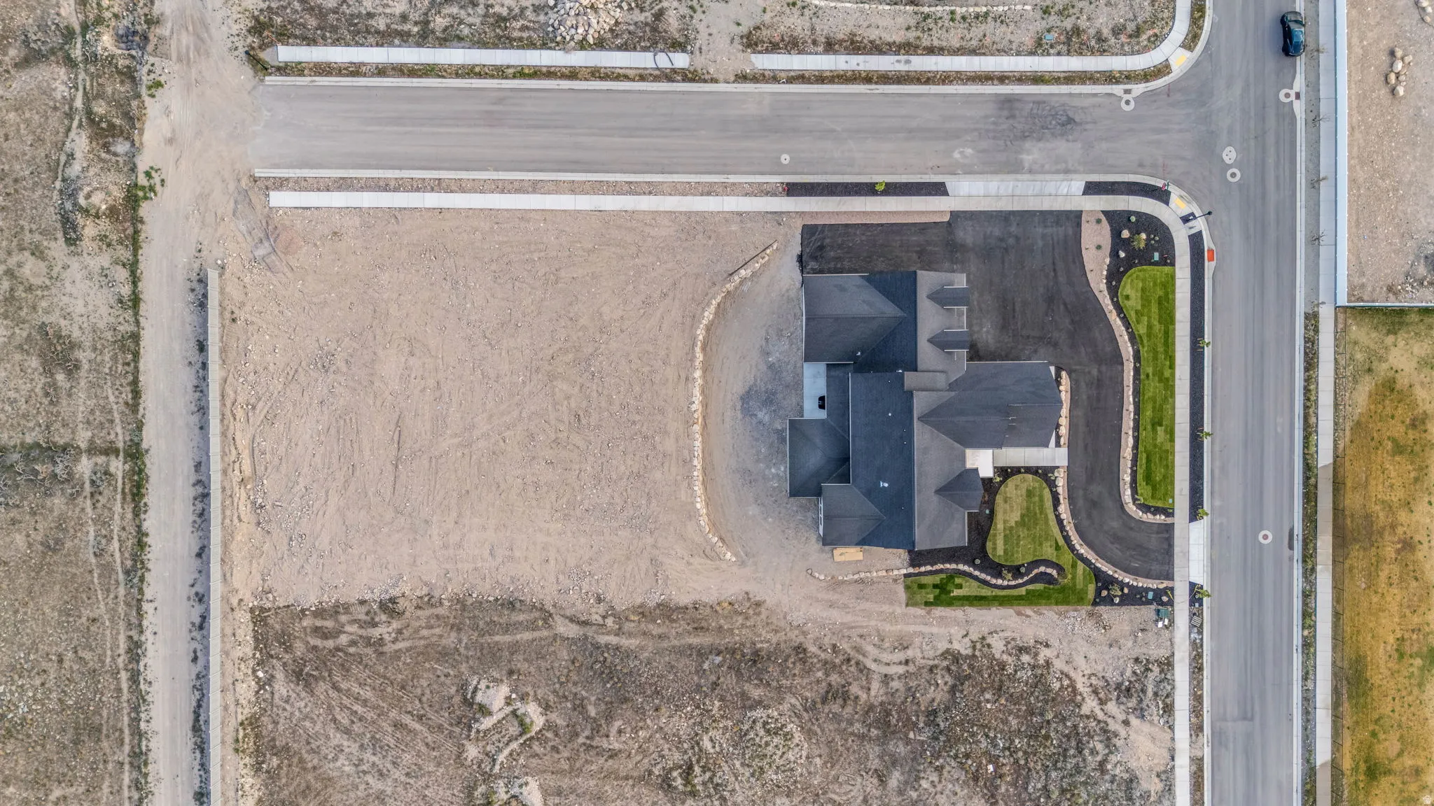 Newly constructed residence featuring a dark shingle roof, established landscaping, paved driveway, and concrete sidewalk