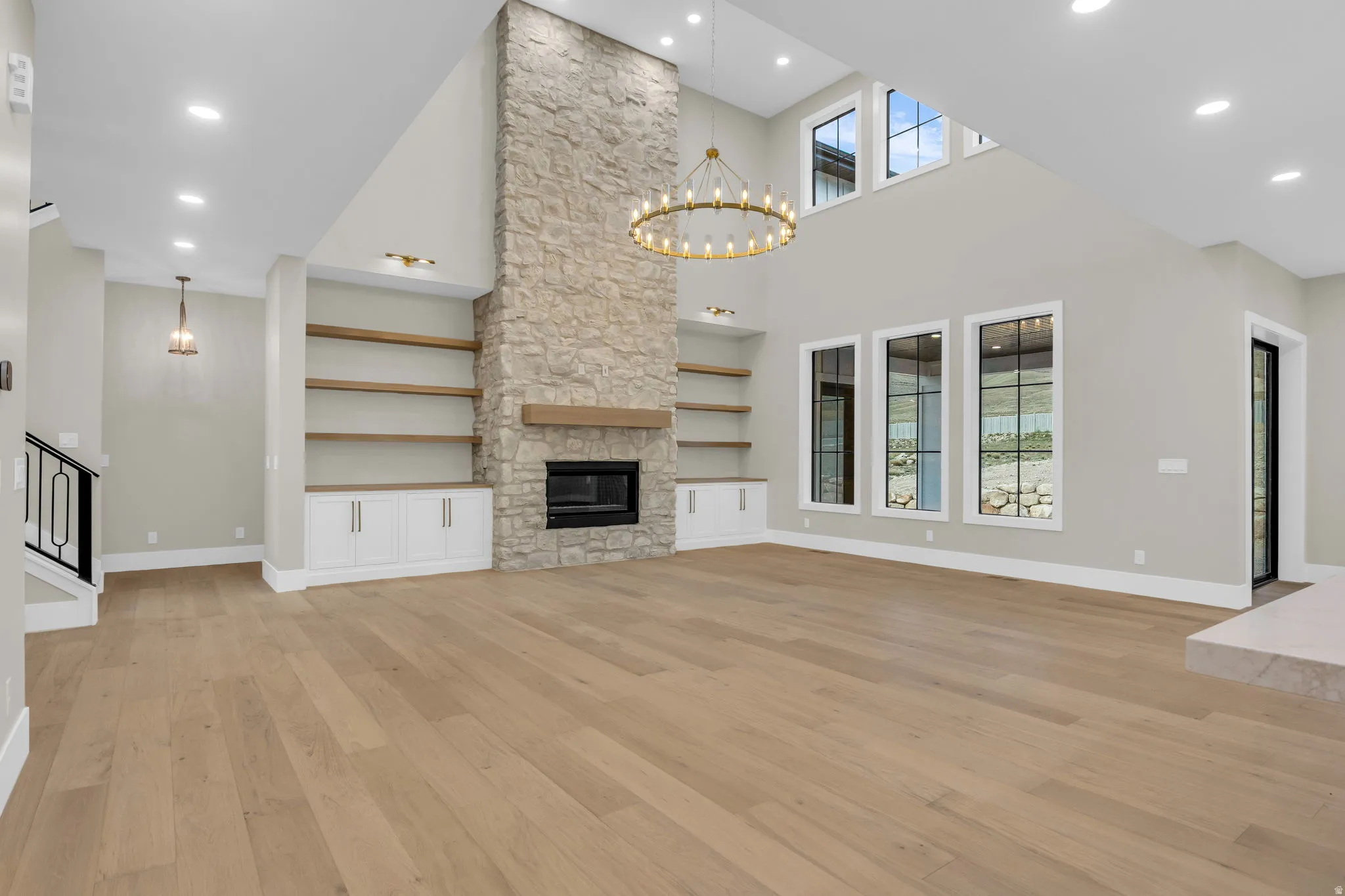 Spacious living area featuring a floor-to-ceiling stone fireplace, a gold-finish chandelier, and wood-finish flooring