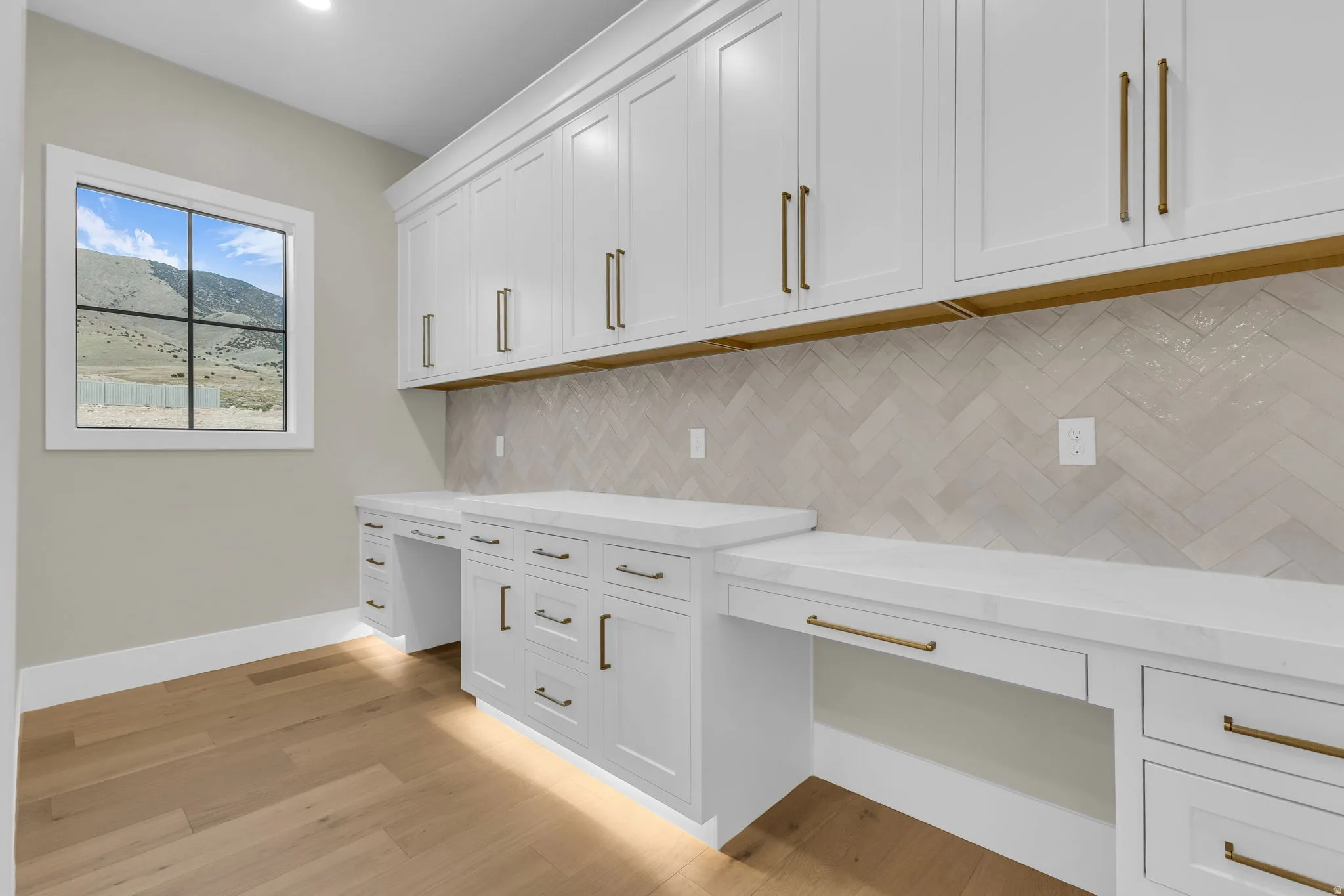Dedicated workspace featuring built-in white shaker cabinetry, white countertops, and a herringbone-patterned tile backsplash