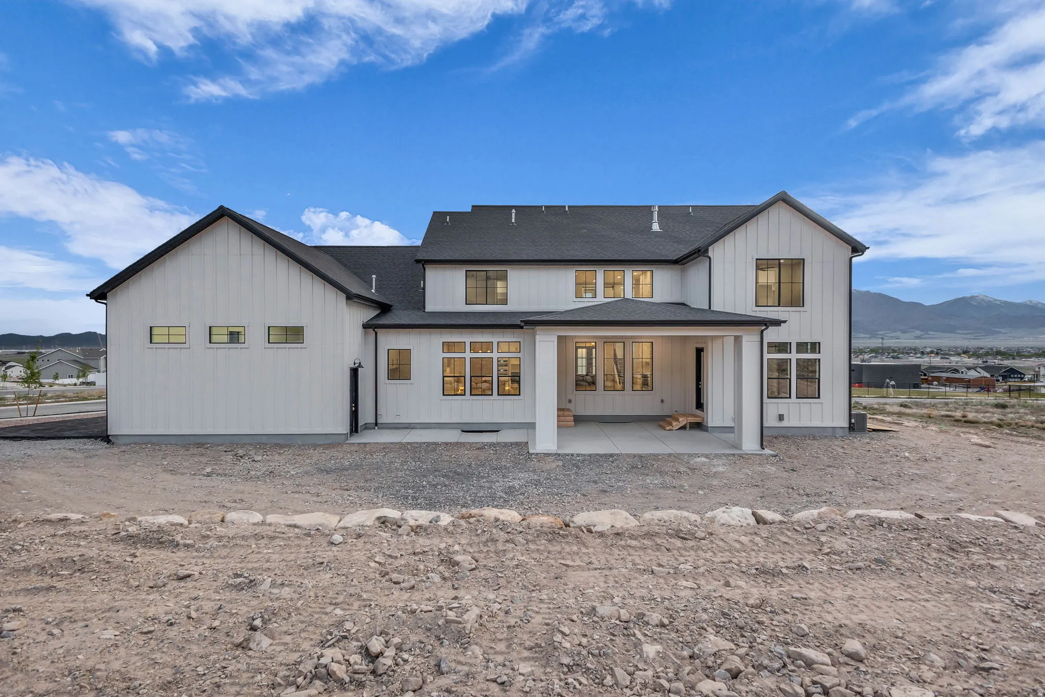 Modern farmhouse architecture featuring white vertical siding, black-framed windows, a covered patio, and a dark shingled roof