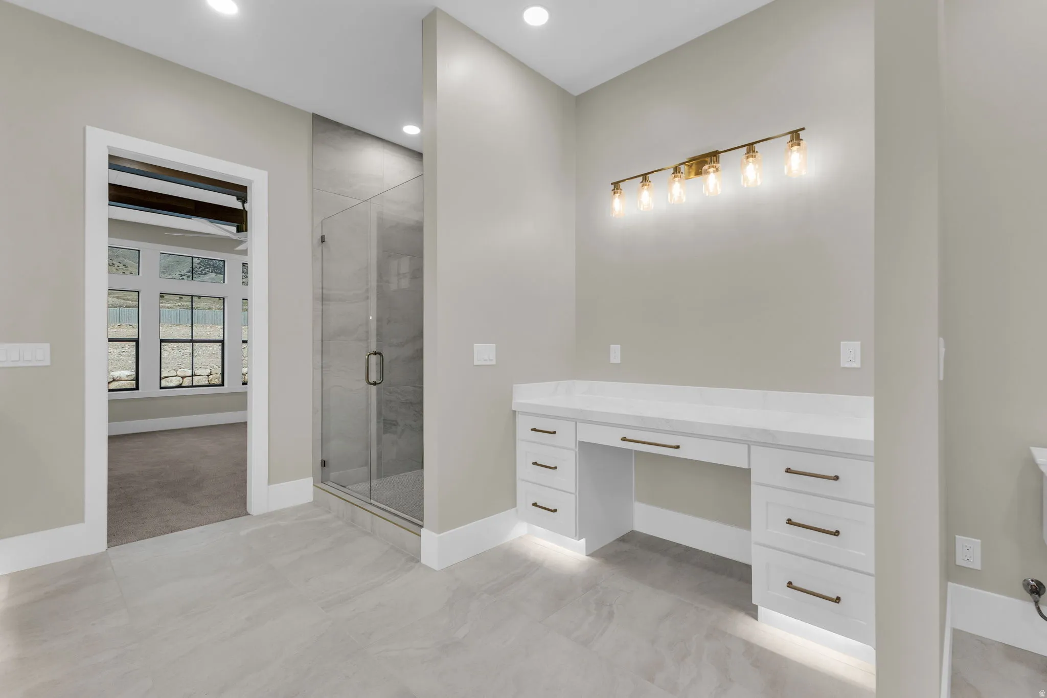 Spacious bathroom featuring a built-in vanity with a light-colored countertop, white cabinetry with dark hardware, and a multi-bulb light fixture