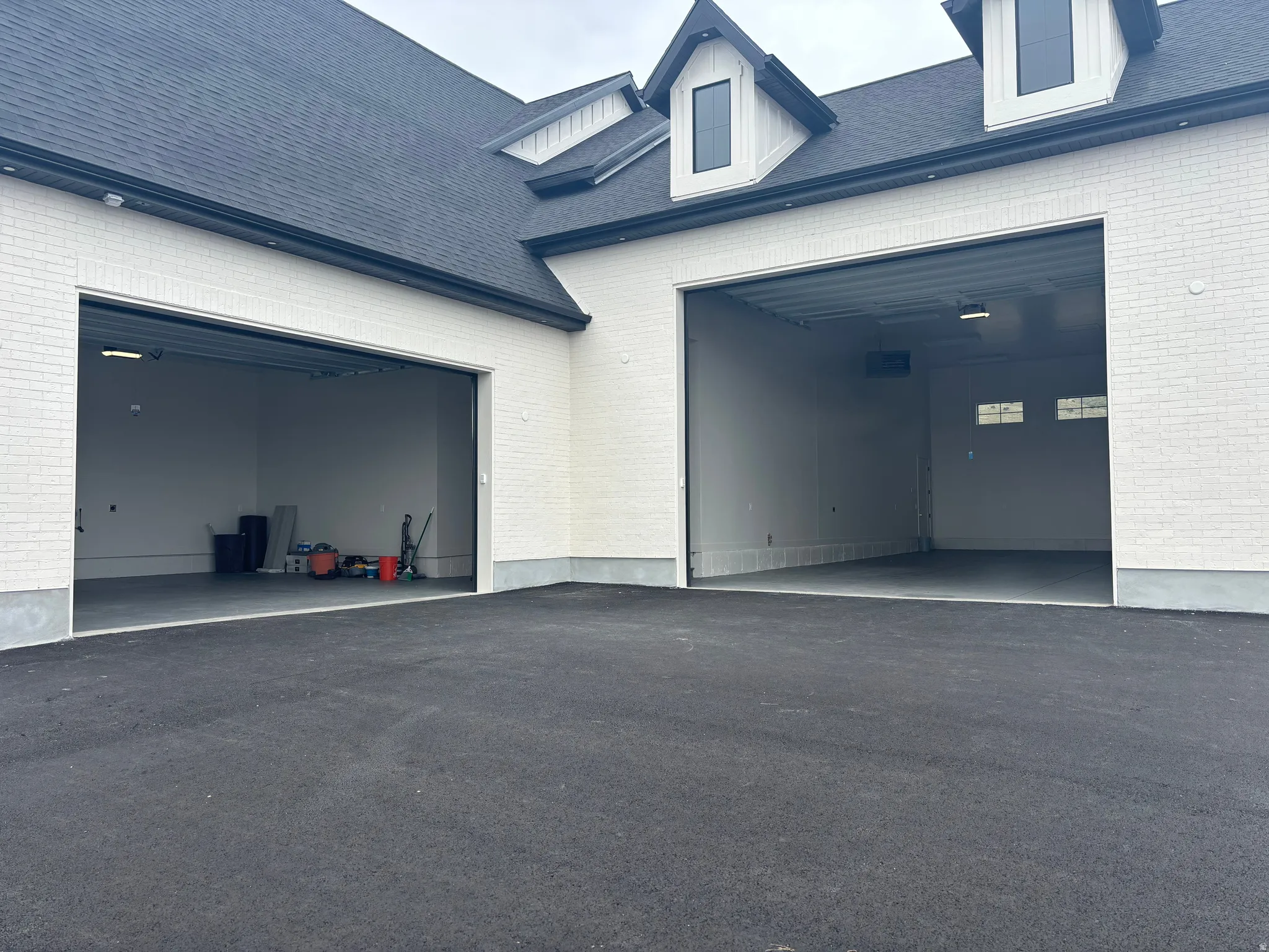 Exterior featuring white brick siding, a dark asphalt shingle roof, and a multi-car garage with two open bays