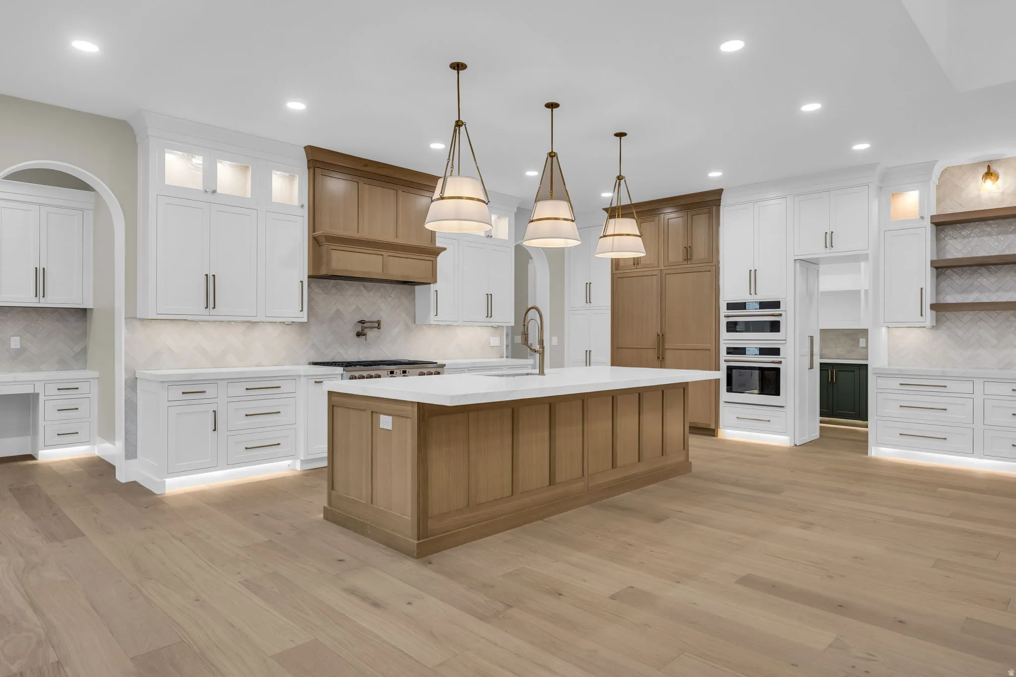 Expansive kitchen featuring a large central island with a light wood-finish base and light-toned countertop, complemented by three pendant light fixtures