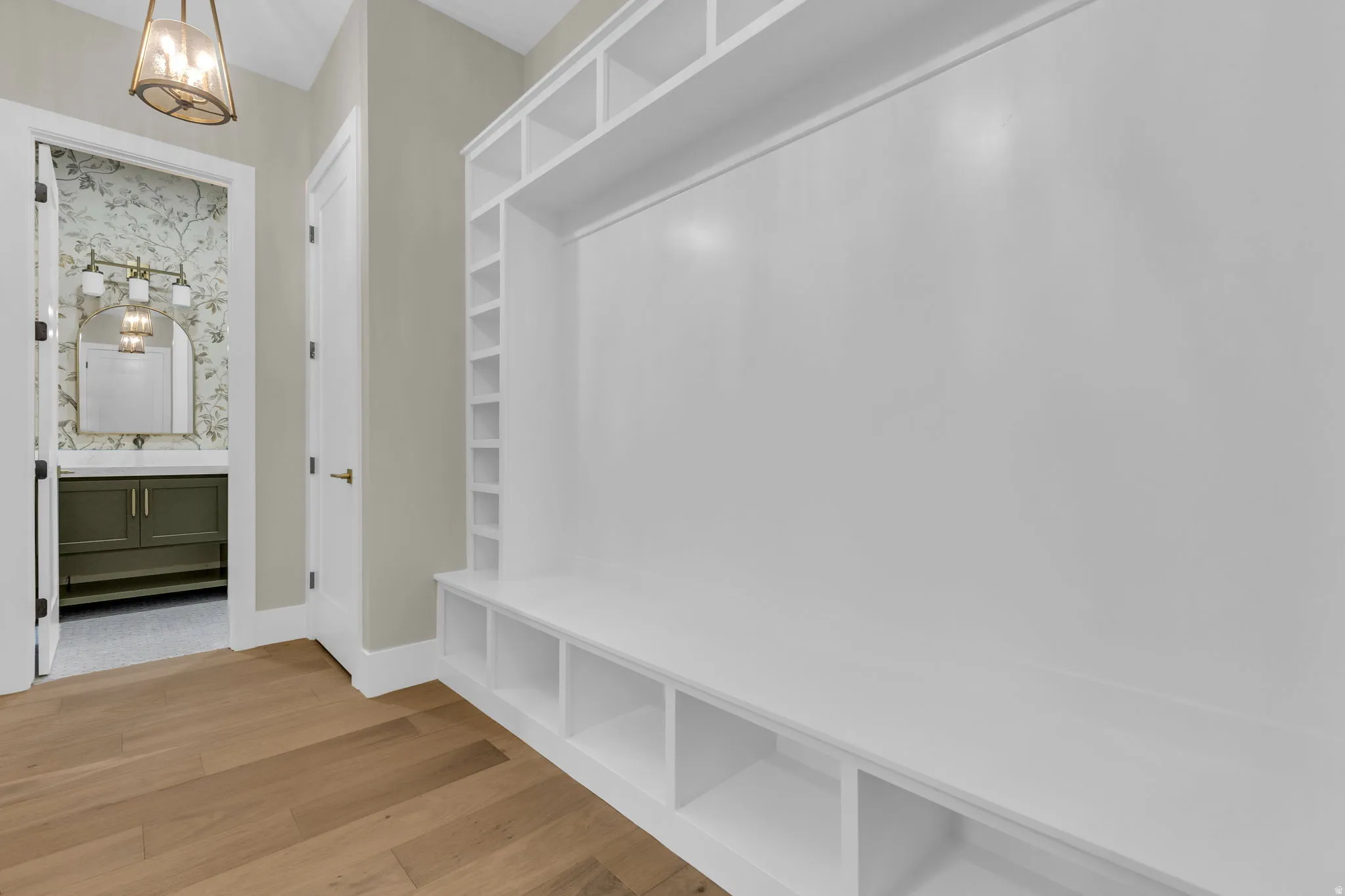 Built-in white storage unit with shelving and bench seating, wood-finish flooring, and a decorative pendant light fixture