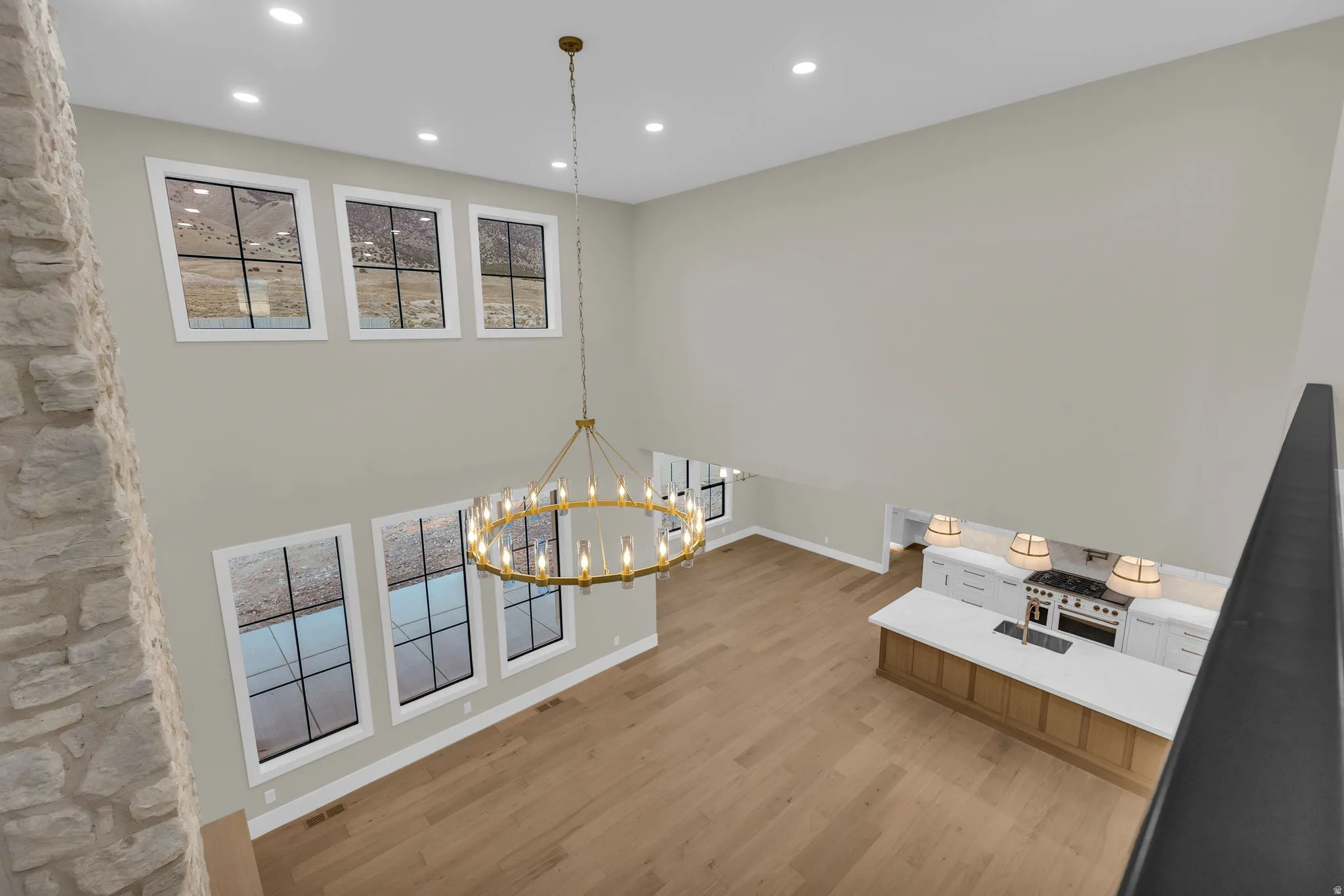 Vaulted living space with a brass chandelier, upper and lower transom windows, a stone-clad column, and wide plank wood-finish flooring