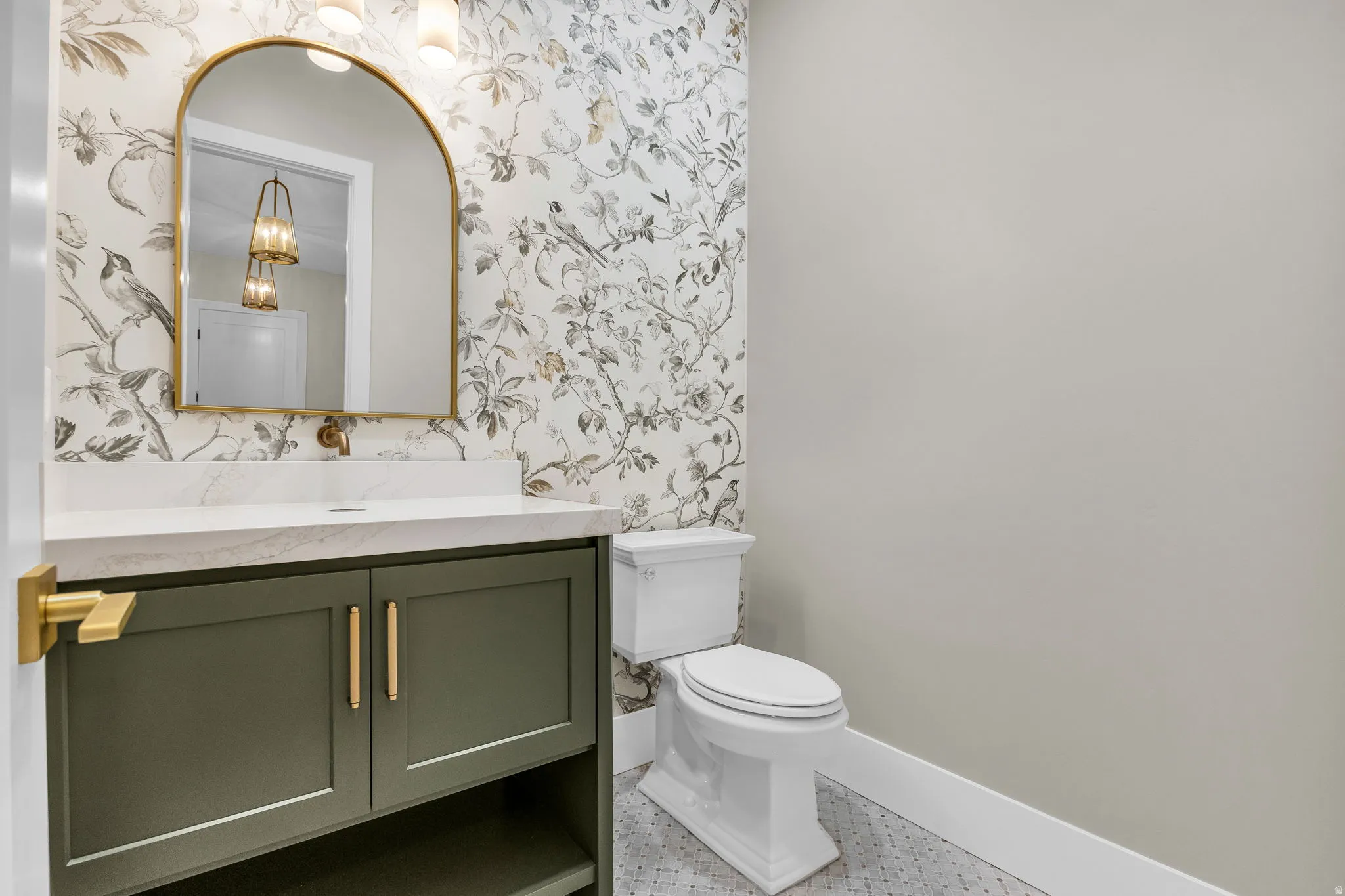 Powder room featuring a sage green vanity with gold hardware, a white countertop, and an arched gold-framed mirror
