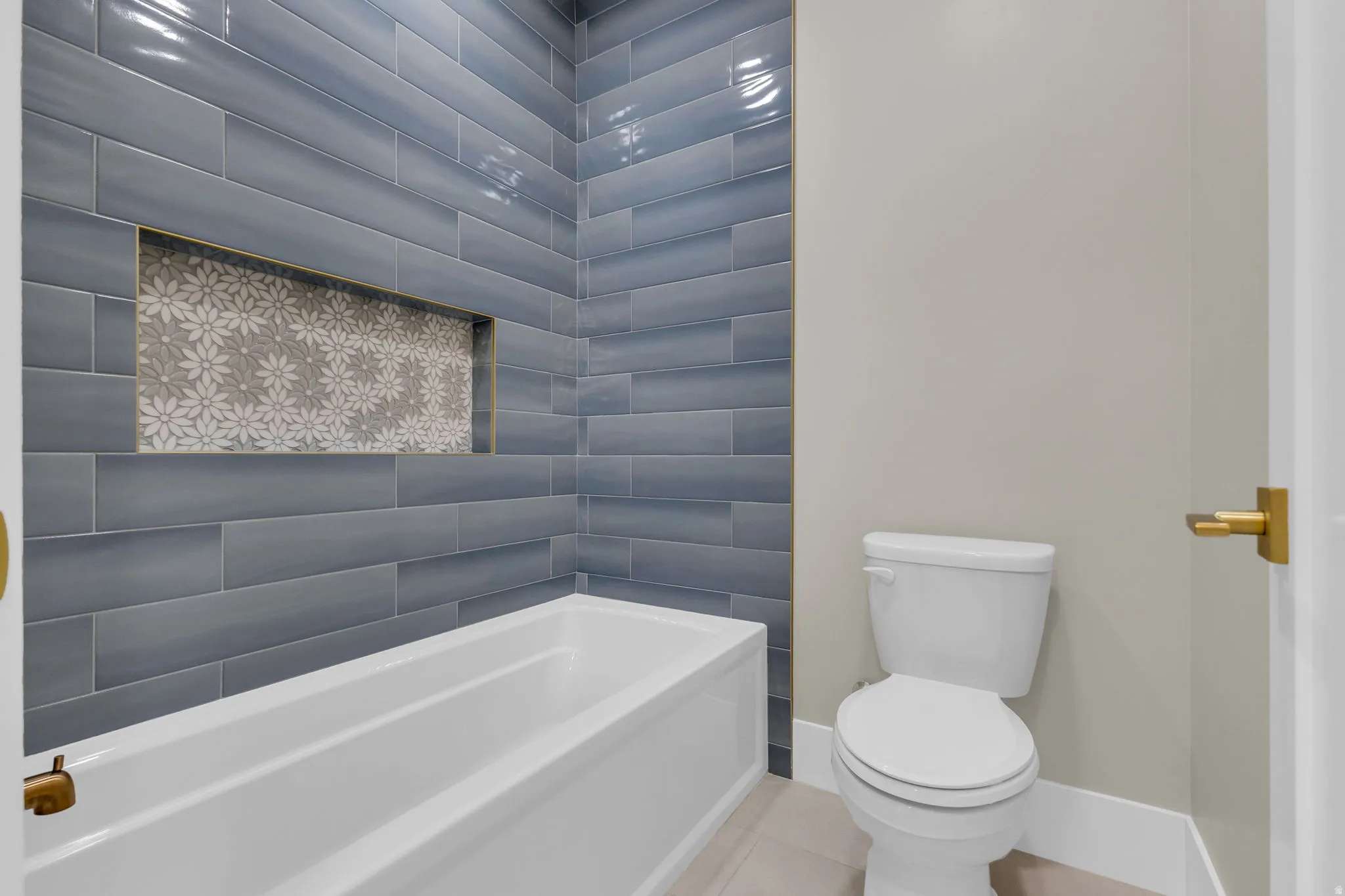 Bathtub with blue subway tile surround featuring a decorative mosaic niche