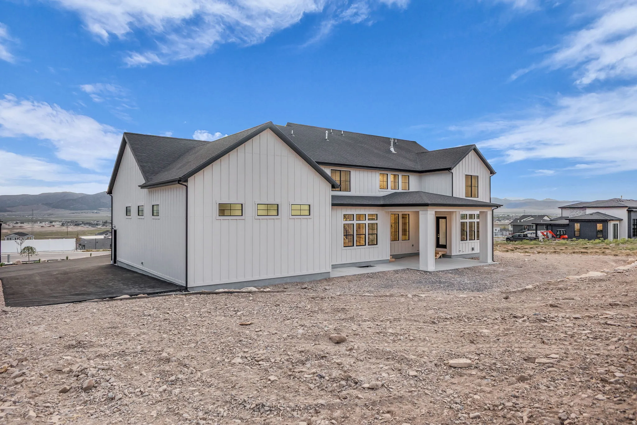 Modern farmhouse-style residence featuring white vertical siding, black-trimmed windows, a covered patio, and dark shingle roofing