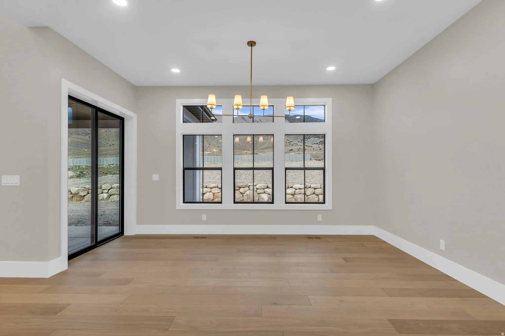 Spacious interior room featuring light wood-finish flooring, recessed lighting, and a modern chandelier