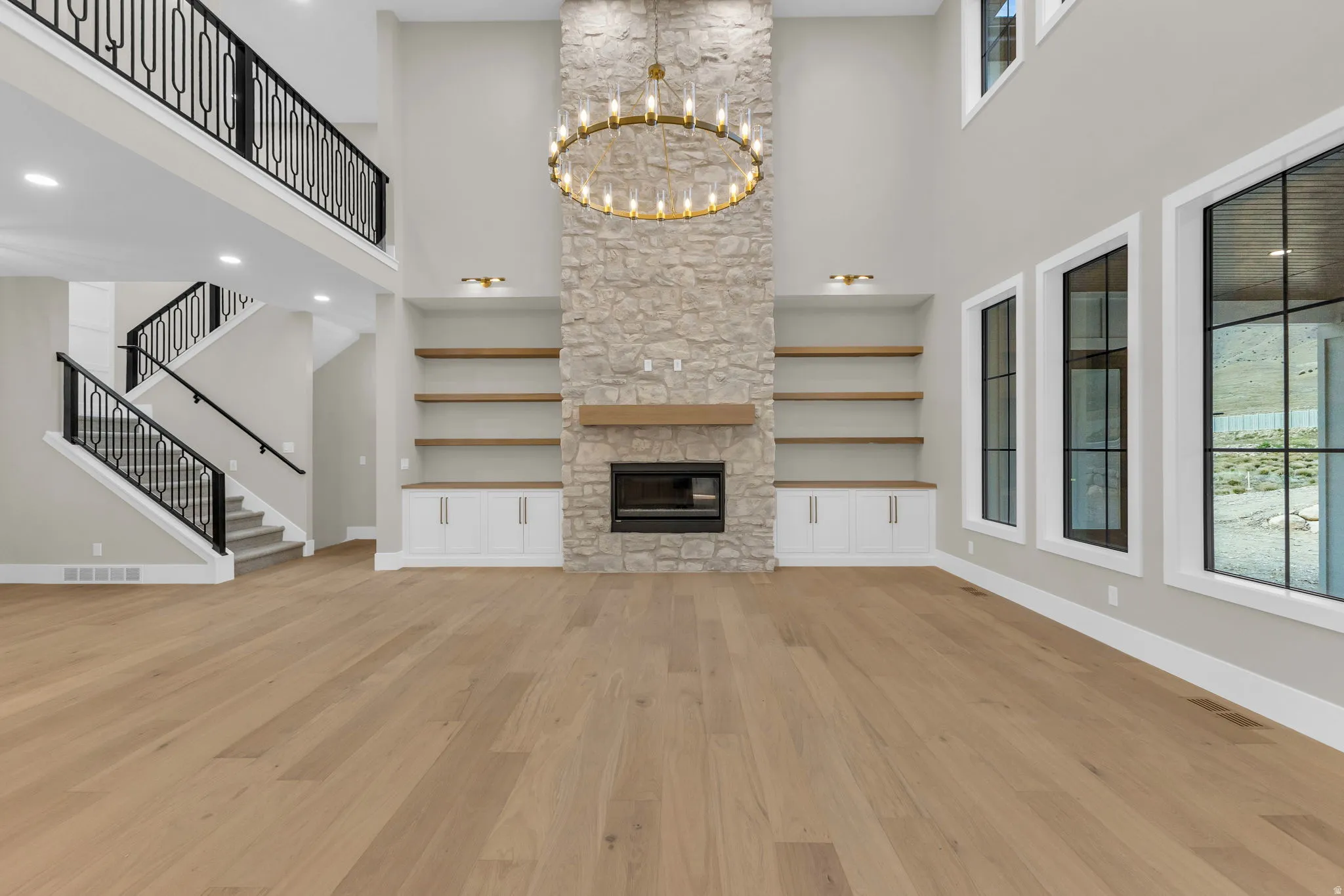 Soaring ceilings featuring a stone fireplace with a wood mantle and built-in shelving
