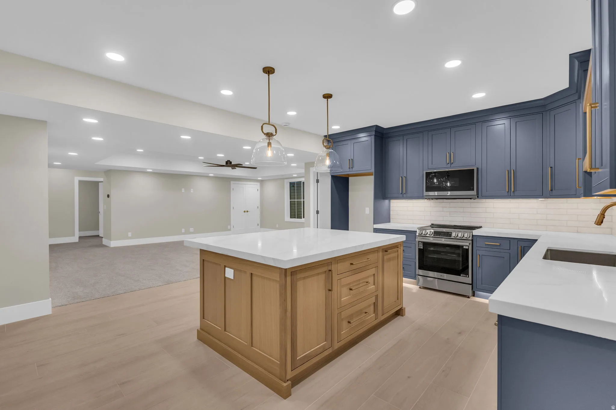Contemporary kitchen featuring blue shaker-style cabinetry, a light wood-finish island with a white countertop, and stainless steel appliances