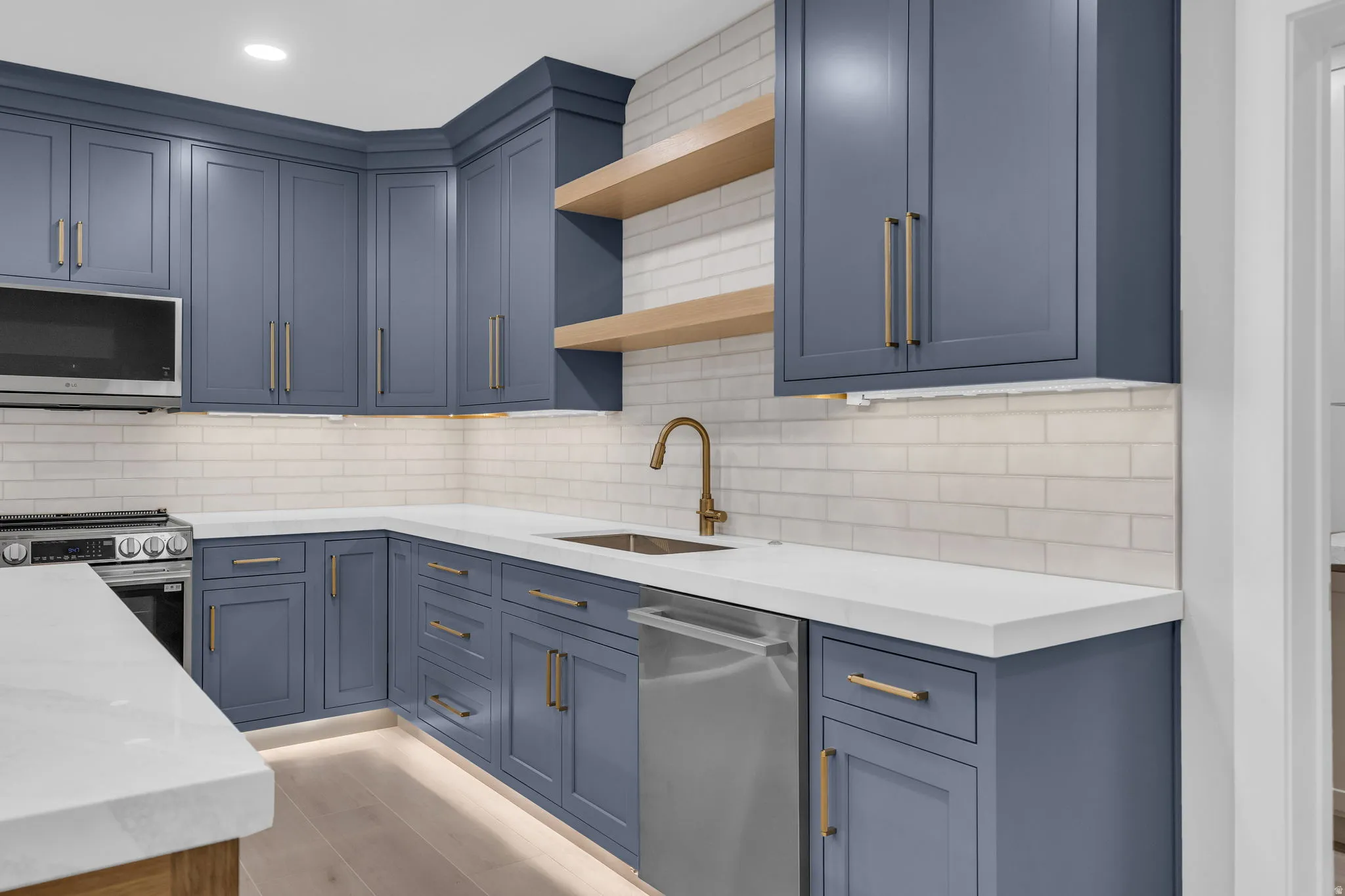 Kitchen featuring blue cabinetry with brass hardware, white subway tile backsplash, white countertops, stainless steel appliances, and integrated shelving