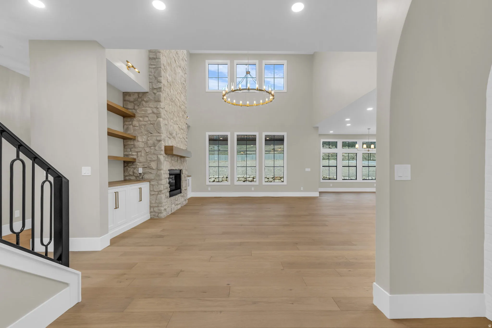 Spacious open-concept living area featuring a stone-clad fireplace with a wooden mantel, custom built-in cabinetry, and floating shelves