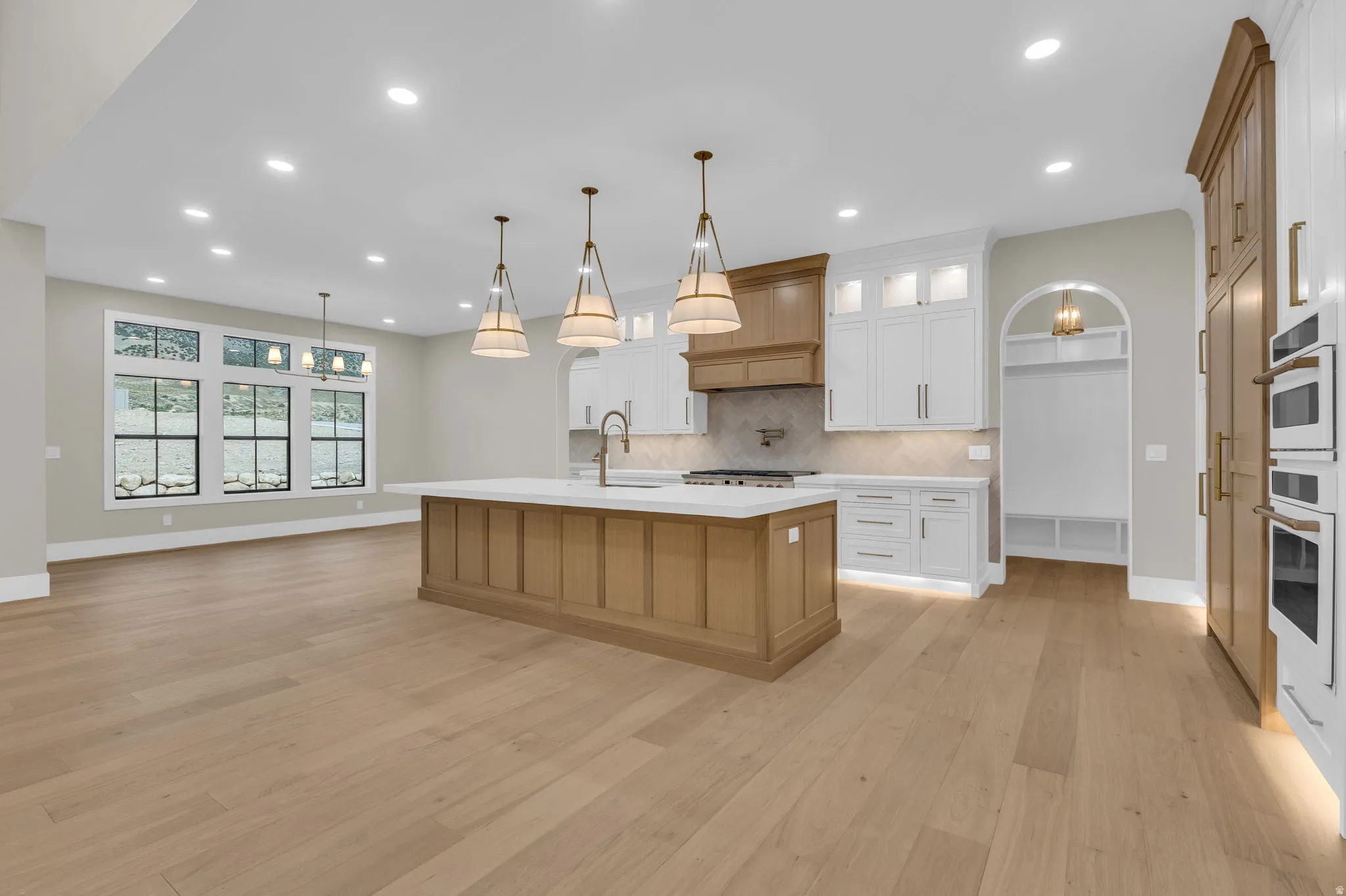 Open-concept kitchen featuring a large central island with a solid surface countertop, light wood-finish flooring, two-tone cabinetry, and integrated double ovens