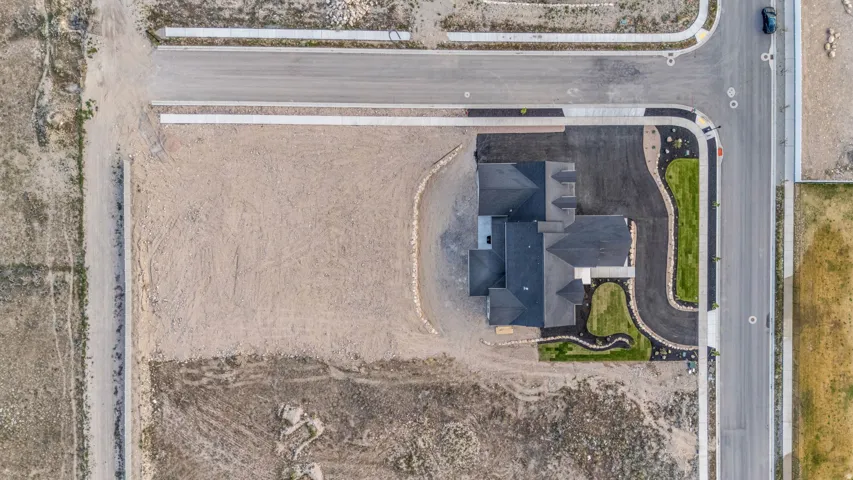 Newly constructed residence featuring a dark shingle roof, established landscaping, paved driveway, and concrete sidewalk