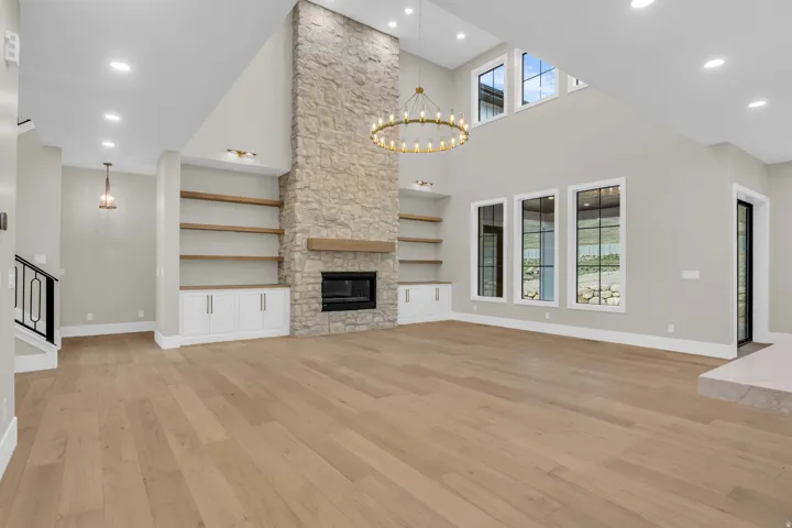 Spacious living area featuring a floor-to-ceiling stone fireplace, a gold-finish chandelier, and wood-finish flooring