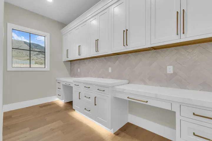 Dedicated workspace featuring built-in white shaker cabinetry, white countertops, and a herringbone-patterned tile backsplash