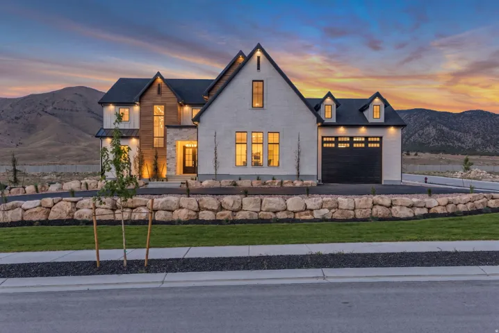 Modern farmhouse exterior featuring an attached two-car garage, stone retaining walls, a paved driveway, and established landscaping
